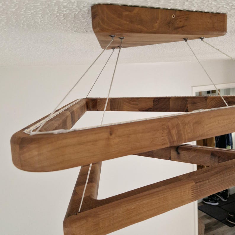 May include: A wooden pendant light fixture with a square frame design. The light is suspended from the ceiling by four white cords.