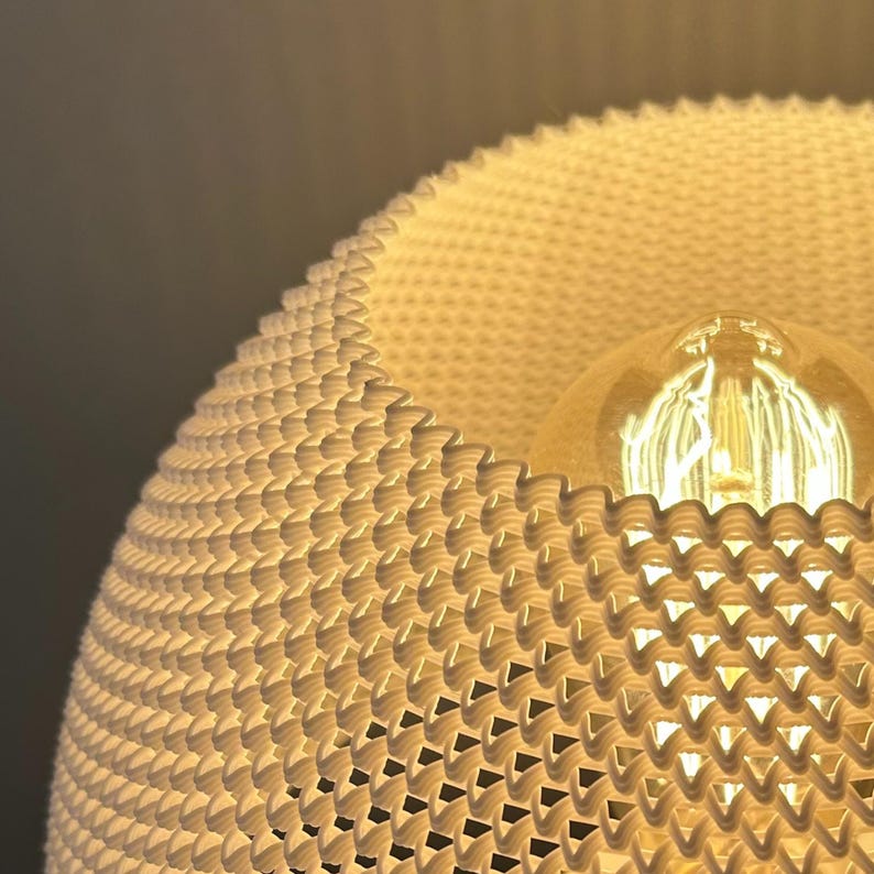 May include: A white, woven lampshade with a geometric pattern. The lampshade is lit from within, casting a warm glow.