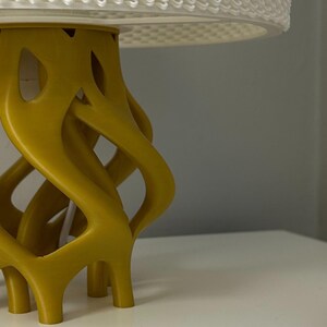 May include: A yellow, 3D printed lamp base with a unique, organic design. The base has a twisted, interwoven pattern and a smooth, matte finish.