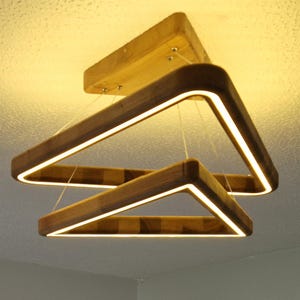 May include: A modern wooden light fixture with two triangular frames. The frames are made of natural wood and have a warm, inviting look. The light fixture is illuminated with warm white LED lights.