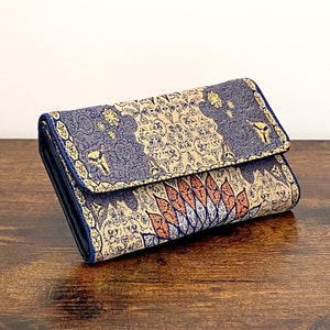 May include: A blue and gold patterned wallet with a floral design. The wallet is closed and lying on a wooden surface.