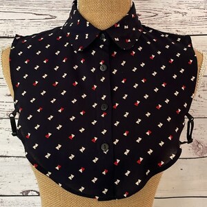 May include: A black faux collar with a white and red geometric pattern. The collar has a button closure and is made of a lightweight fabric.