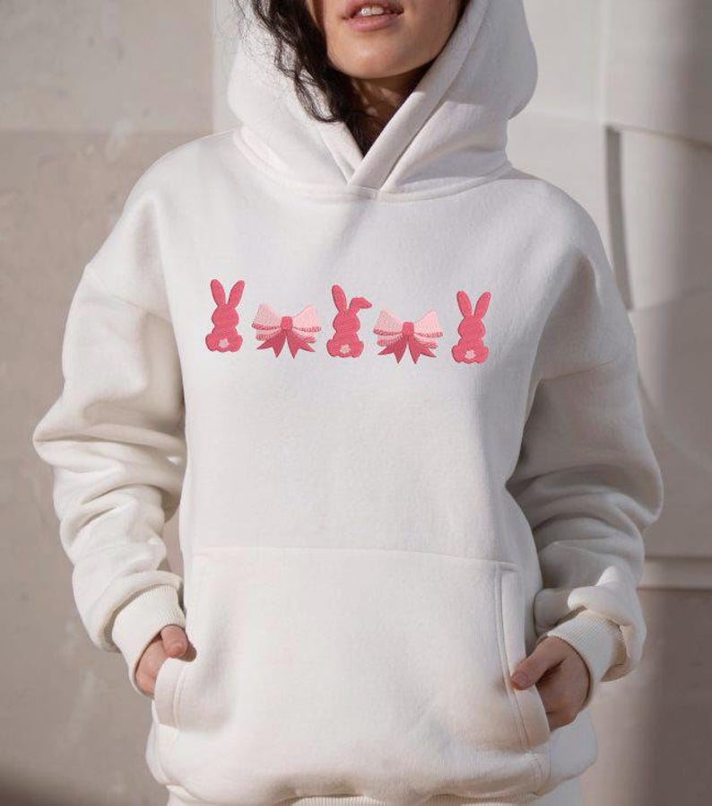 Op de afbeelding: Witte hoodie met een roze geborduurd ontwerp van konijntjes met strikjes.