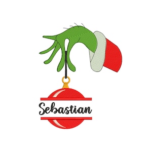 May include: A green hand with a red Santa hat holds a red Christmas ornament with the name Sebastian written on it.