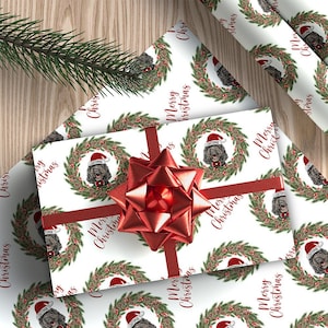 May include: White wrapping paper with a repeating pattern of a dog wearing a Santa hat in a wreath with red berries and pine branches. The text "Merry Christmas" is repeated throughout the paper.