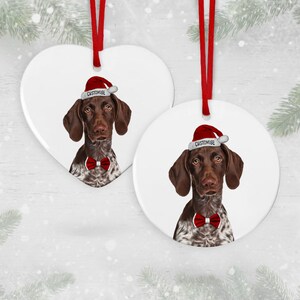 May include: Two ceramic Christmas decorations featuring a German Shorthaired Pointer dog wearing a Santa hat and a red bow tie. The decorations are white with the text "CUSTOMISE" on each.