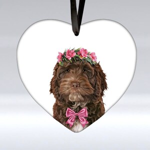 May include: A brown and white dog wearing a pink flower crown and a pink bow tie. The dog is on a white heart-shaped background.