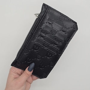 May include: Black cardholder with a zipper closure and embossed geometric patterns. The wallet has multiple card slots and a zippered compartment. The design features repeating circular and star-like shapes.