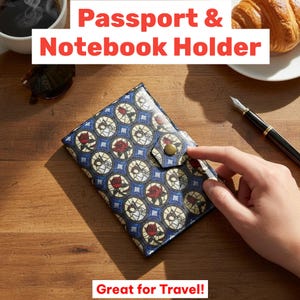 May include: A blue passport and notebook holder with a decorative pattern of red roses and circular designs. The text "Passport & Notebook Holder" and "Great for Travel!" are displayed. The holder is closed with a snap.
