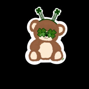 May include: A brown teddy bear wearing green shamrock glasses and a green shamrock headband.