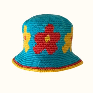 Könnte beinhalten: Ein blauer gehäkelter Bucket-Hut mit roten und gelben Blumen. Der Hut hat eine breite Krempe und einen gelben Besatz.