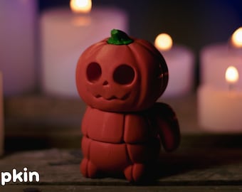 以下が含まれることがあります： 小さな赤いセグメント化されたカボチャで、ジャック・オ・ランタンの顔が彫られています。カボチャは、燃えているろうそくの列の前にある木製の表面の上に置かれています。