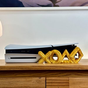 May include: A white gaming console with a gold XOXO sign on a wooden table with two drawers.