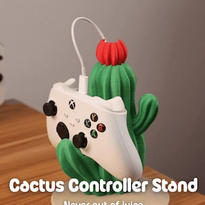 May include: A green cactus-shaped controller stand with a red flower top, holding a white game controller. The stand has the text "Cactus Controller Stand" and "Never out of juice".