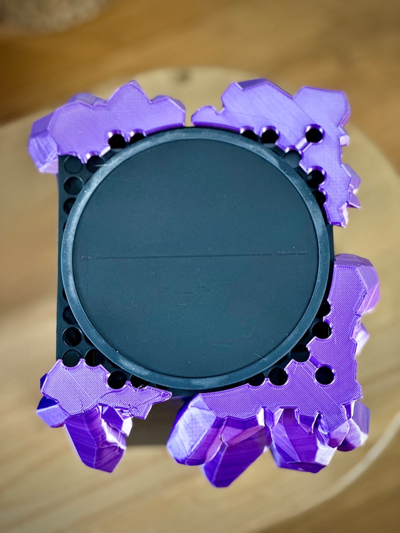 May include: A purple 3D printed crystal-shaped stand with a black circular base. The stand has a textured surface and is designed to hold a small object.