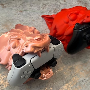 May include: Two 3D printed wolf head game controller holders. One is a red wolf head holding a black Xbox controller. The other is a copper wolf head holding a white Playstation controller.
