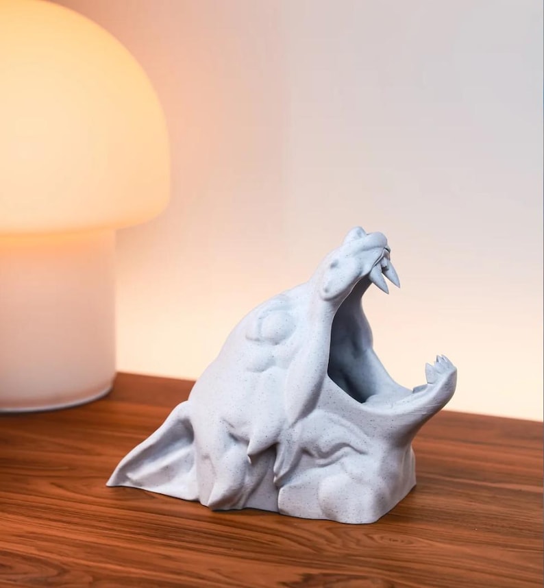 May include: A white ceramic sculpture of a wolf's head with its mouth open, revealing sharp teeth. The sculpture is on a wooden surface.