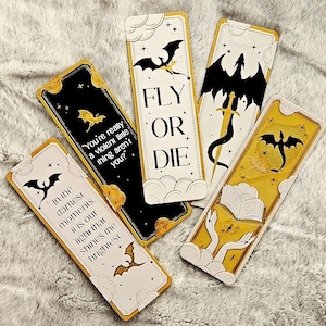 Puede incluir: Cinco marcadores decorativos con diseños de dragones y nubes. Los marcadores presentan colores negro, dorado y blanco. Un marcador dice "FLY OR DIE". Otro dice "You're really a violent little thing aren't you?"
