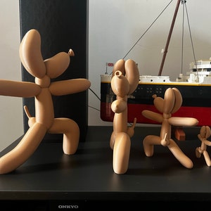 May include: Four balloon animal sculptures in various poses. The sculptures are made of a light brown material and are arranged on a black surface.