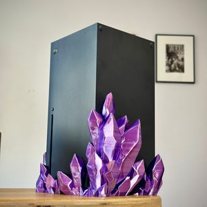 May include: A black gaming console sits on a purple crystal stand. The console is on a wooden table.