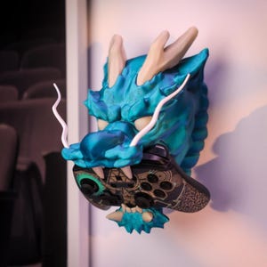 May include: A teal blue dragon head wall mount with white horns and a black and gold video game controller in its mouth.