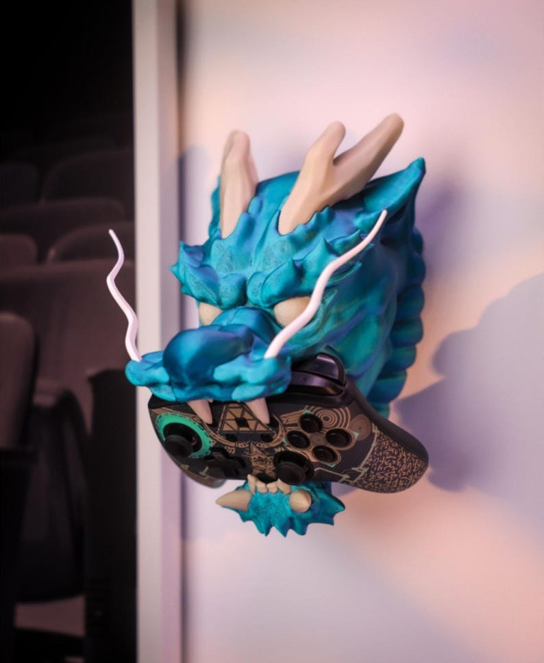 May include: A teal blue dragon head wall mount with white horns and a black and gold video game controller in its mouth.