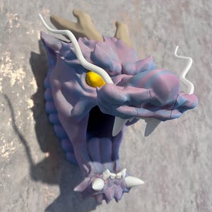 May include: Purple and blue dragon head wall sculpture with white horns and a yellow eye. The dragon's mouth is open and has white teeth.