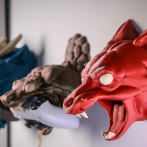 May include: Three 3D printed animal head wall mounts. A red wolf head with a white eye, a brown dragon head with a white eye, and a blue dragon head.