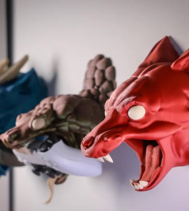 May include: Three 3D printed animal head wall mounts. A red wolf head with a white eye, a brown dragon head with a white eye, and a blue dragon head.