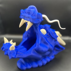 May include: A blue 3D printed dragon head sculpture with white teeth and a white horn. The dragon's mouth is open and the sculpture is sitting on a black surface.