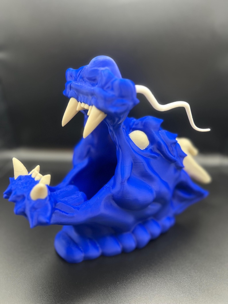 May include: A blue 3D printed dragon head sculpture with white teeth and a white horn. The dragon's mouth is open and the sculpture is sitting on a black surface.
