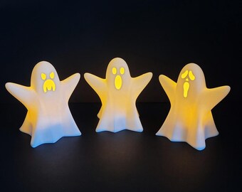 May include: Three white ghost figurines with glowing yellow faces. The ghosts are in a variety of poses with their arms outstretched.