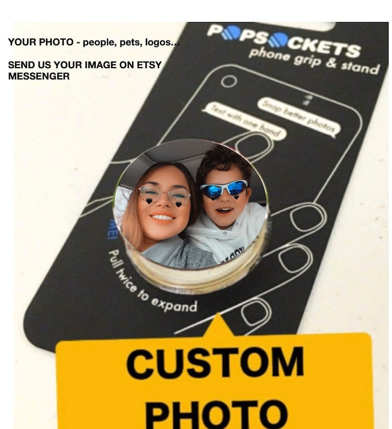 Puede incluir: Una agarradera de tel&eacute;fono y un soporte para tel&eacute;fono personalizados con fondo negro. La agarradera de tel&eacute;fono presenta una carcasa redonda de pl&aacute;stico transparente con una foto de una mujer y un ni&ntilde;o. El texto "POPSOCKETS phone grip & stand" est&aacute; impreso en blanco sobre el fondo negro. El texto "CUSTOM PHOTO" est&aacute; impreso en blanco sobre un fondo amarillo.
