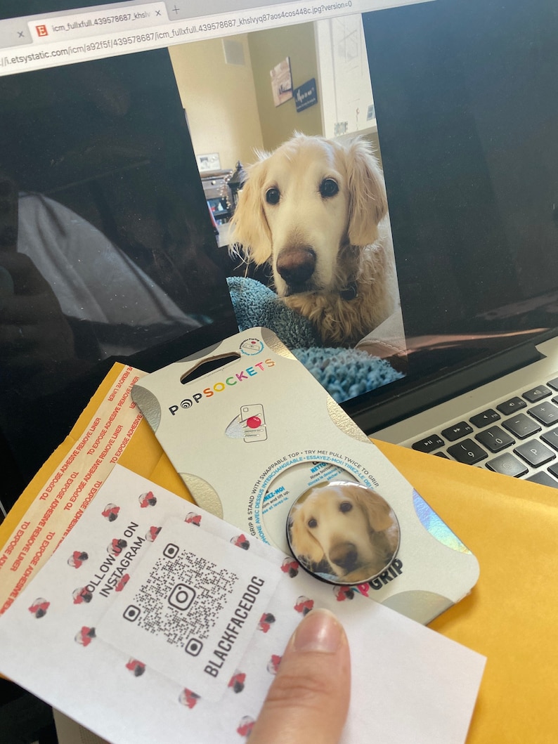 Puede incluir: Una agarradera de tel&eacute;fono blanca y dorada con una imagen de un perro golden retriever. La agarradera es redonda y tiene un anillo negro alrededor del borde. El texto "BLACKFACEDOG" est&aacute; impreso en la tarjeta blanca debajo de la agarradera. El texto "FOLLOW US ON INSTAGRAM" est&aacute; impreso en la tarjeta blanca encima de la agarradera. Un c&oacute;digo QR est&aacute; impreso en la tarjeta blanca.