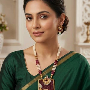 Puede incluir: Un conjunto de collar y pendientes dorados con un colgante rectangular y pendientes cuadrados a juego. Las joyas están adornadas con paneles texturizados de color granate, hilos de cuentas blancas y piedras verde claro en forma de gota.