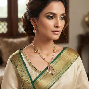 May include: A gold necklace featuring a central pendant with red and green stones and small white pearls, paired with matching drop earrings. The jewelry is worn with a cream-colored garment that has a wide, ornate green and gold border.