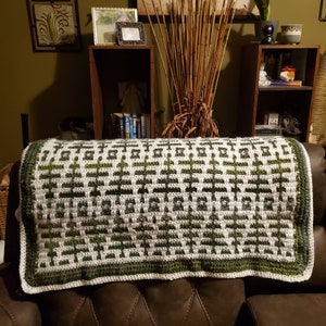 May include: A green and white crocheted throw blanket with a geometric pattern. The blanket is draped over a brown leather couch.