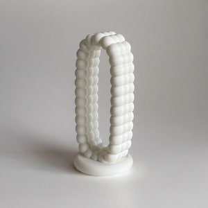 Puede incluir: Escultura de cerámica blanca con un diseño redondeado y texturado. La escultura tiene forma de arco alto y estrecho.