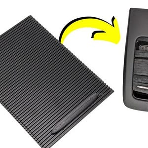 Op de afbeelding: Een zwarte rubberen mat met een getextureerd oppervlak en een klein zwart handvat. De mat is ontworpen om in de middenconsole van een auto te passen.