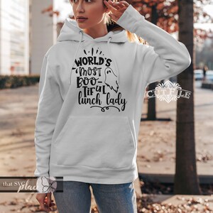 K&ouml;nnte beinhalten: Ein wei&szlig;er Kapuzenpullover mit schwarzem Text, der "World's Most Boo-tiful Lunch Lady" lautet, mit einer Geistergrafik.