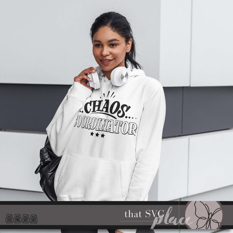 May include: A white hoodie with black text that reads "...CHAOS... COORDINATOR" with three stars below the text. The model is wearing the hoodie and has headphones around her neck.