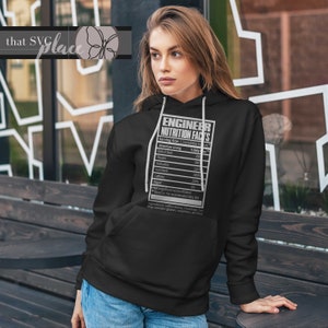 Op de afbeelding: Zwarte hoodie met een witte afbeelding van een voedingswaardelabel voor een ingenieur. Het label vermeldt toewijding, cafe&iuml;ne en spijt als ingredi&euml;nten.
