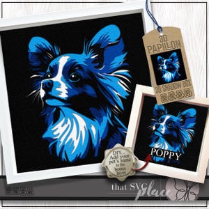 May include: A framed blue and white Papillon dog portrait with the name "Poppy" on a smaller framed image. A tag reads "3D Papillon 3D Shadow Box". The image includes the text "DIY... Add your pet's name to the bonus layer".