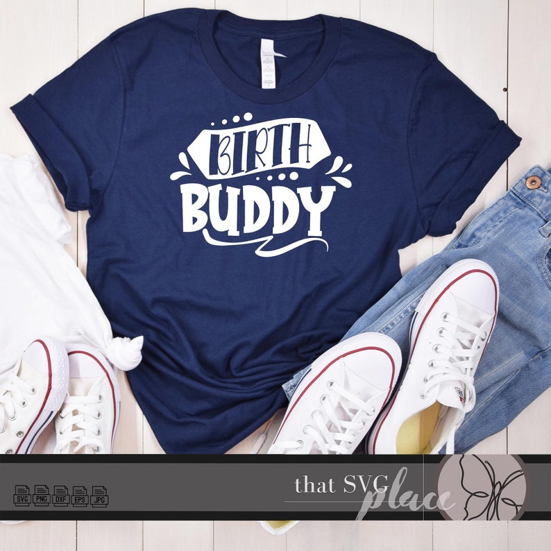 Pu&ograve; includere: Una maglietta blu navy con testo bianco che dice "Birth Buddy". La maglietta &egrave; appoggiata su una superficie di legno bianco con un paio di scarpe da ginnastica bianche e jeans blu.