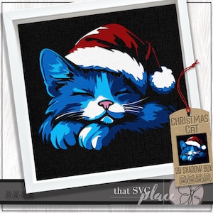 May include: A framed print featuring a blue cat wearing a Santa hat. The cat is depicted with closed eyes and paws crossed, set against a black background. A tag reads "Christmas Cat" with a small image of the cat.