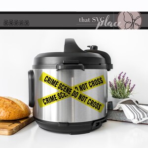 May include: A silver Instant Pot with a black lid and handle. Yellow caution tape is wrapped around the pot with the text "CRIME SCENE DO NOT CROSS" printed on it.