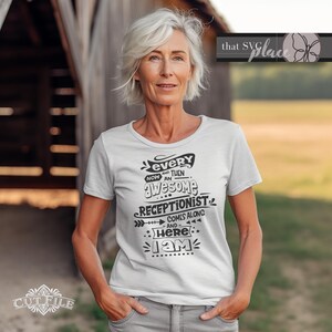 Op de afbeelding: Een wit T-shirt met zwarte tekst die "Every now and then an awesome receptionist comes along and here I am" zegt.