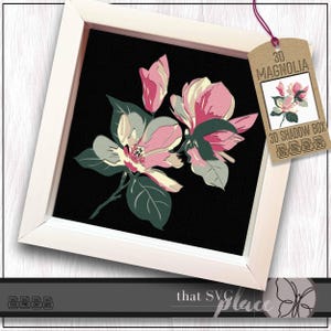 May include: A framed floral art piece featuring a 3D magnolia design. The artwork showcases pink and cream-colored magnolia blossoms with green leaves against a black background. The frame is white, and a tag reads "3D Magnolia".