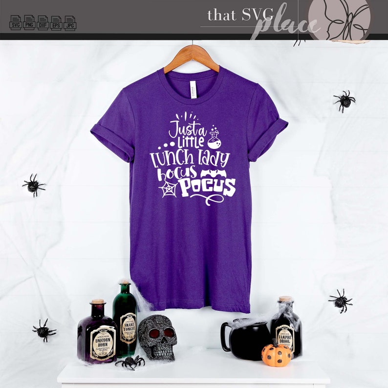 K&ouml;nnte beinhalten: Lilafarbenes T-Shirt mit wei&szlig;em Text, der "Just a little lunch lady Hocus Pocus" lautet, mit einem Spinnennetz und Flederm&auml;usen.