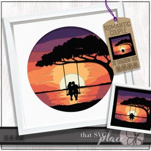 May include: A framed 3D shadow box art piece featuring a romantic sunset scene. The artwork depicts a couple on a swing silhouetted against a vibrant orange and yellow sunset. The tag reads "Romantic Couple 3D Shadow Box".